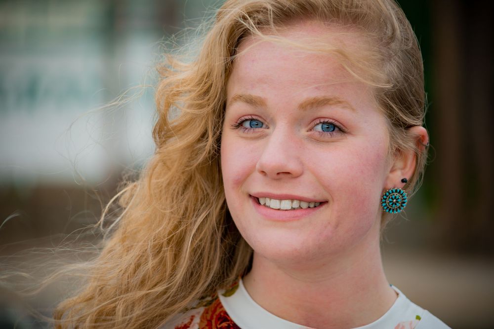 Portrait showing someone with wavy blonde hair wearing earrings against blurred background.