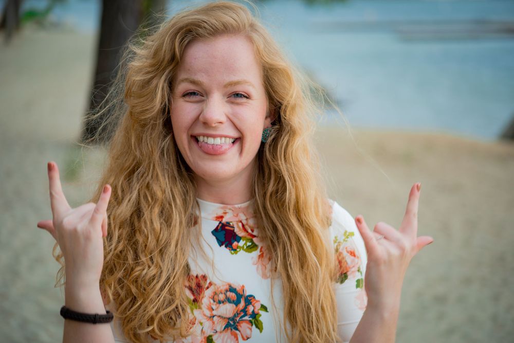 Person with long blonde hair makes rock and roll hand gestures while wearing floral print shirt.