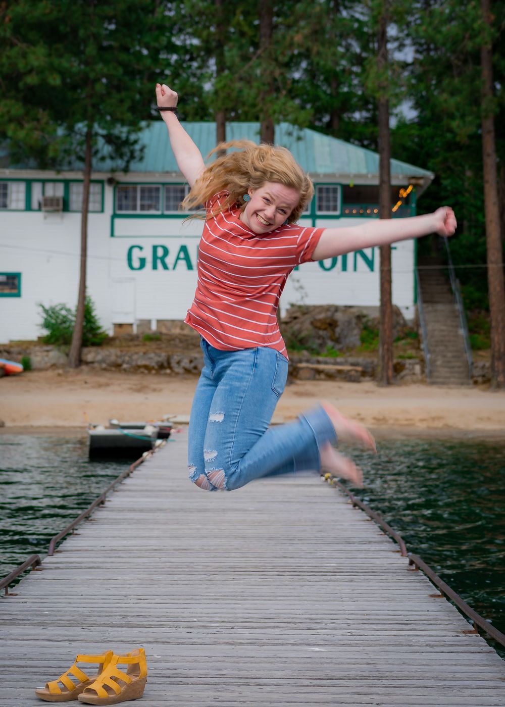 An energetic jump shot on a dock with yellow sandals and a striped shirt.