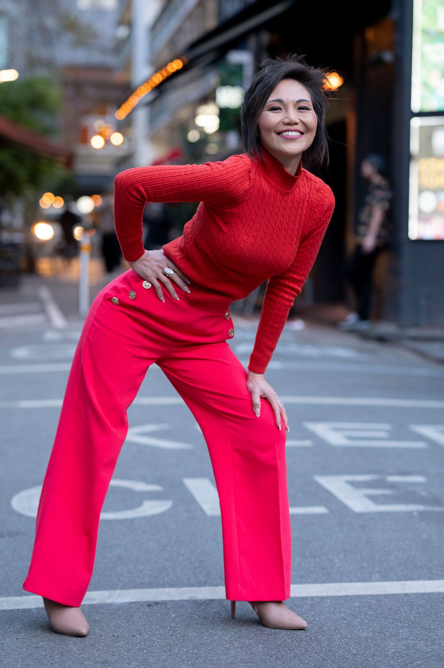 Stylish woman in red turtleneck and pink wide-leg pants poses confidently on a city street.