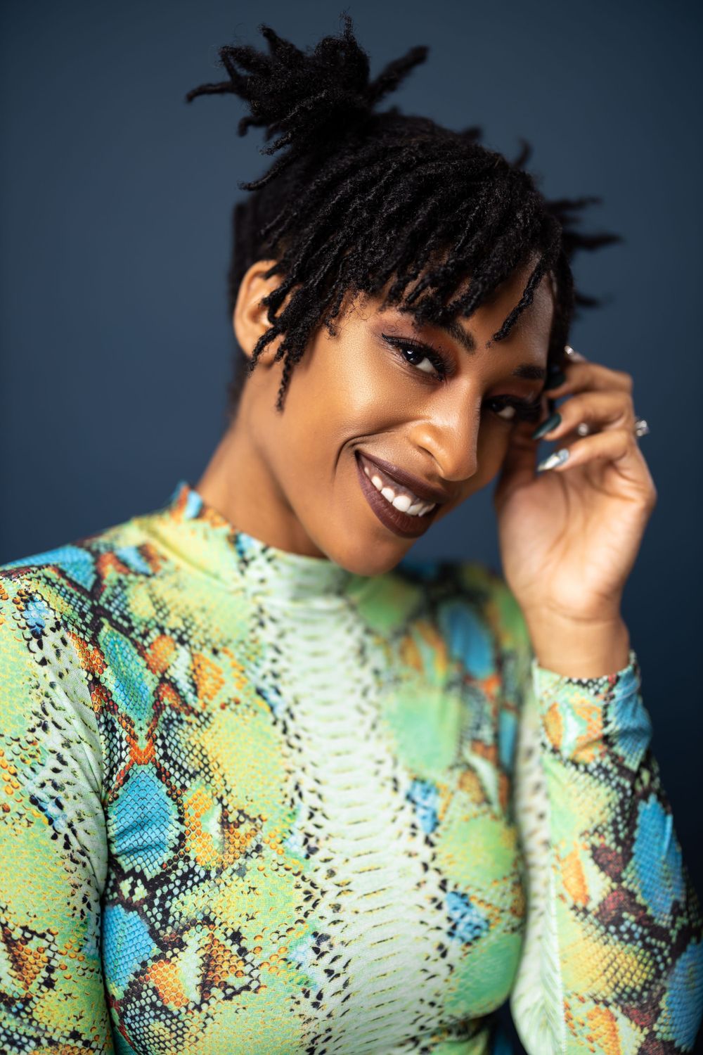 Close up fashion portrait featuring vibrant snakeskin print top against blue background.