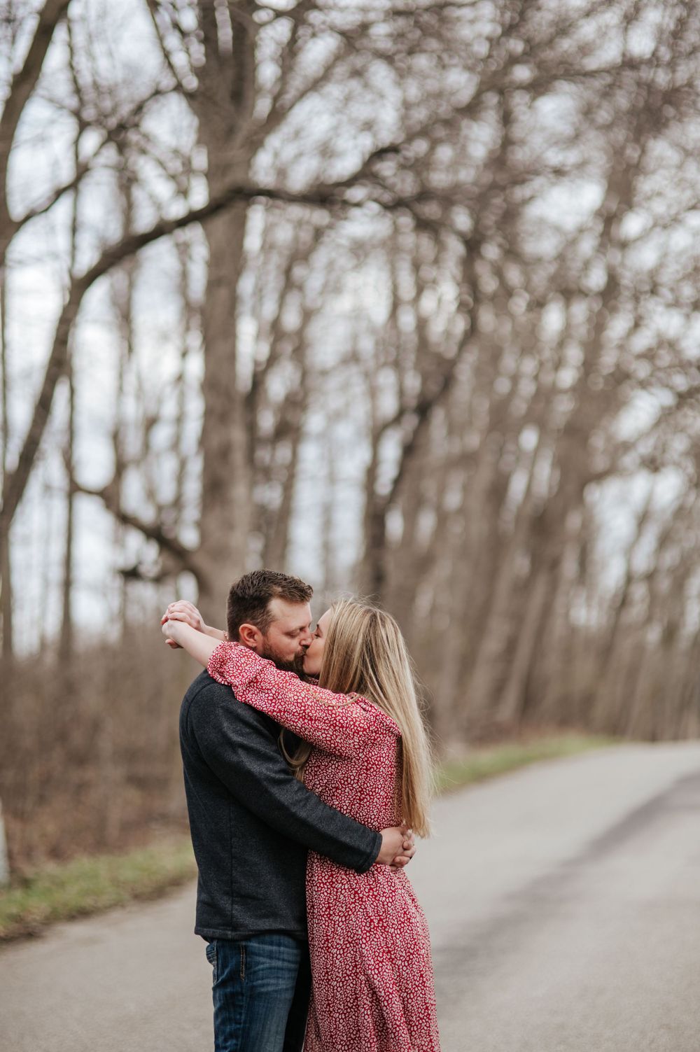 A romantic embrace on a wooded path with person wearing pink dress and dark sweater.