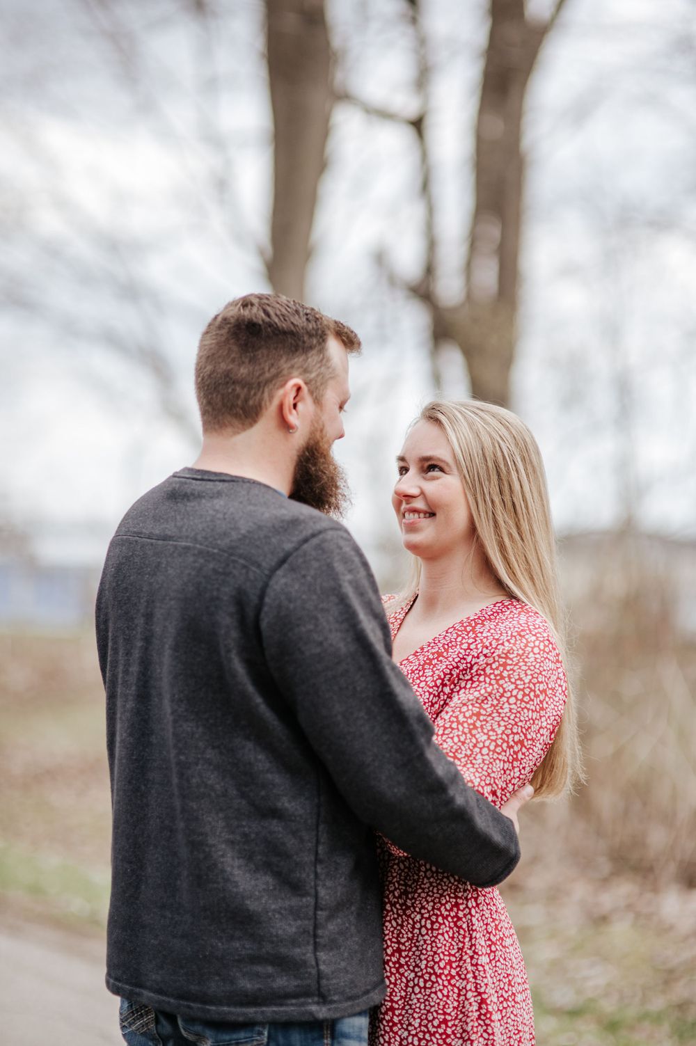 A couple sharing a tender moment outdoors in casual attire against a winter forest backdrop.