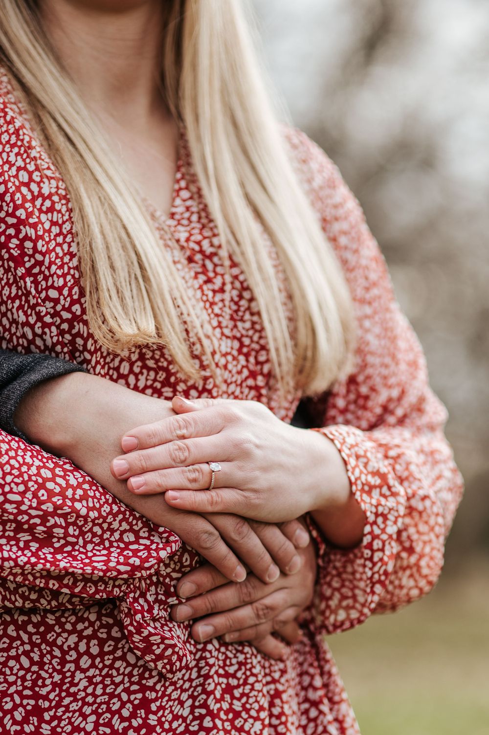 Close-up of hands wearing engagement ring with red floral dress detail.