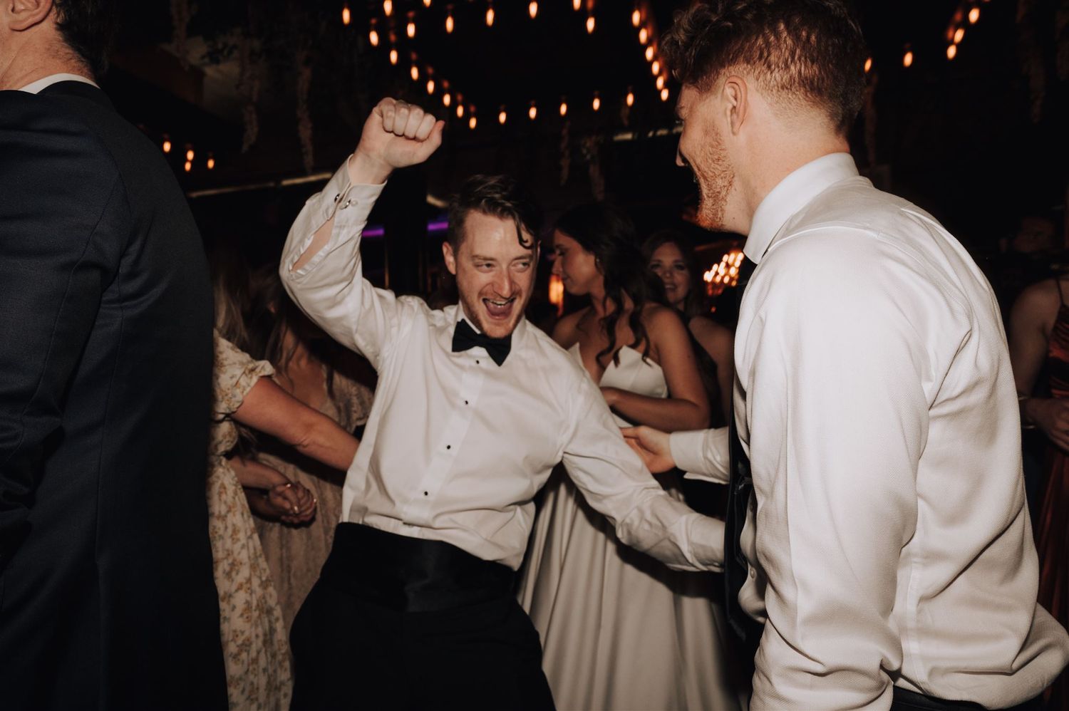 Energetic dancing at a wedding reception with string lights creating a warm atmosphere.