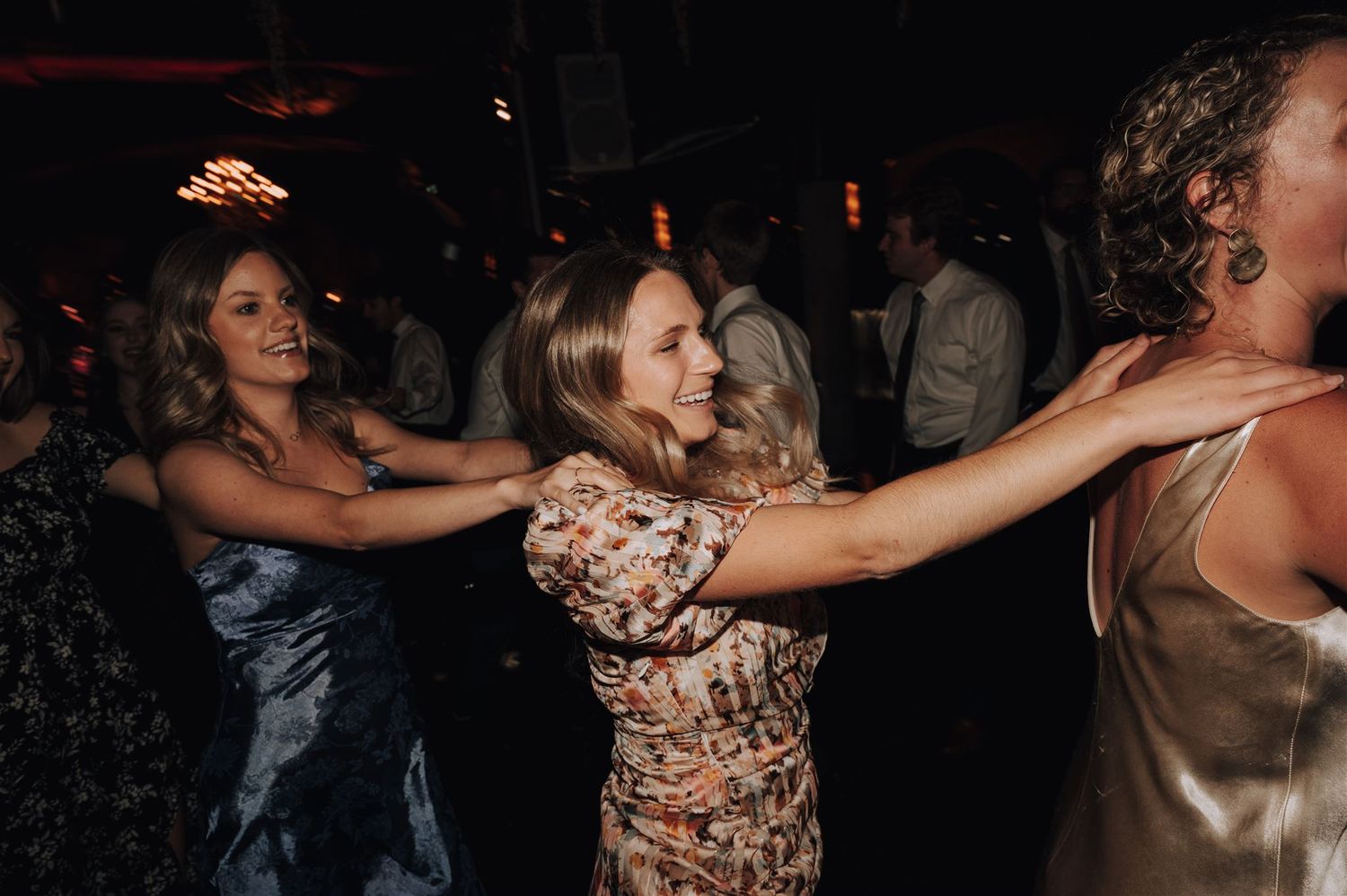 Wedding guests forming a dance chain in elegant dresses at an evening reception.