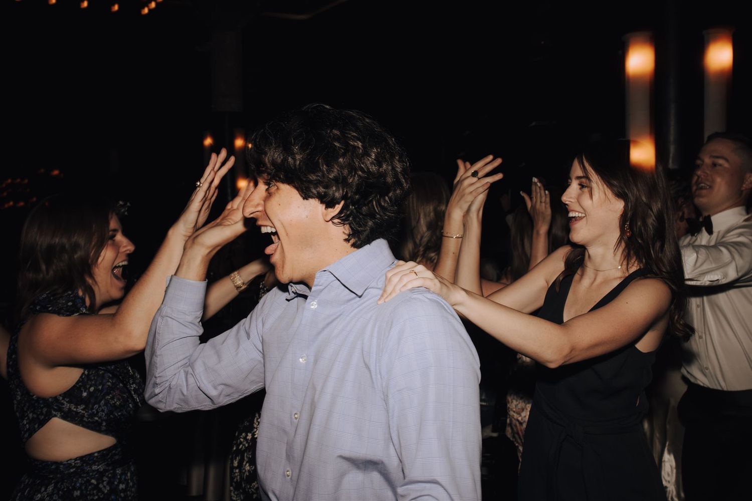 Enthusiastic party guests dancing with hands in the air under moody lighting.