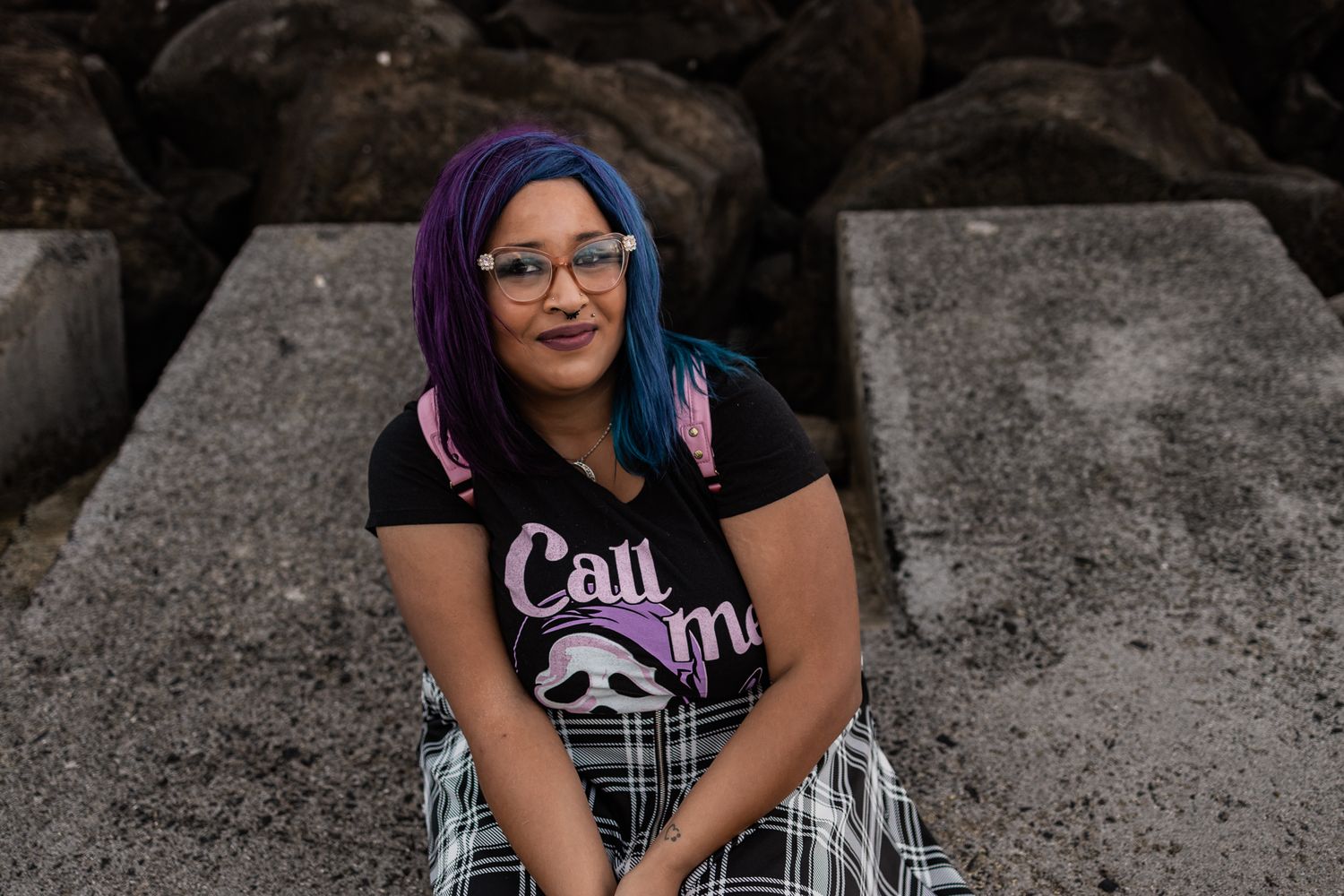 Person with colorful hair wearing glasses sits on concrete blocks.