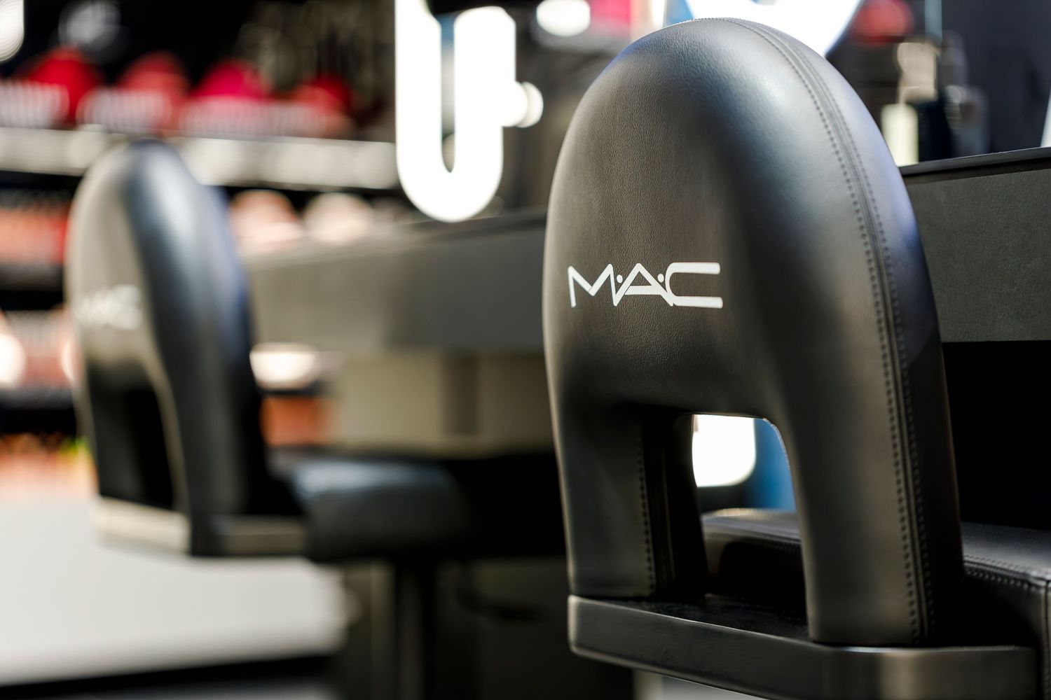 Close-up of black MAC branded makeup station chairs in store.