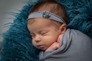 Peaceful sleeping baby on blue fur with gray headband.