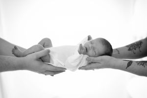 A black and white photo of gently cradled newborn baby lying on white fabric.