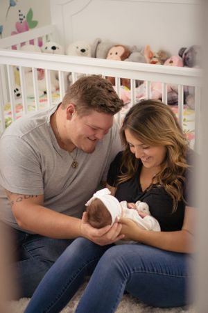 New parents sharing intimate moment with newborn baby in nursery with stuffed animals.