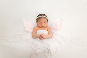 Sleeping newborn with pink wings and tiara on white backdrop.