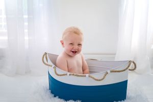 Baby sits in blue and white nautical themed boat prop during photoshoot.