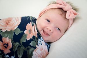 Baby in pink bow and floral dress smiling against white background.