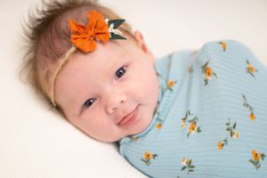Baby wearing orange bow on floral blue outfit.