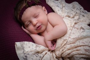 Sleeping baby with lace headband on burgundy fabric.
