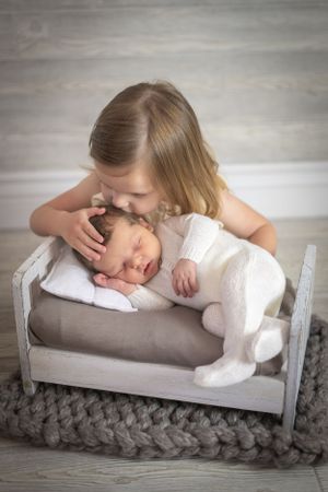 Sweet sibling moment captured on small wooden bed with knitted blanket.