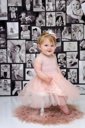 Baby in pink tulle dress and tiara poses against backdrop of black and white baby photos.