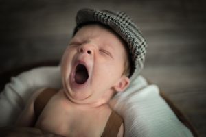 Yawning baby wearing a newsboy cap in black and white portrait.