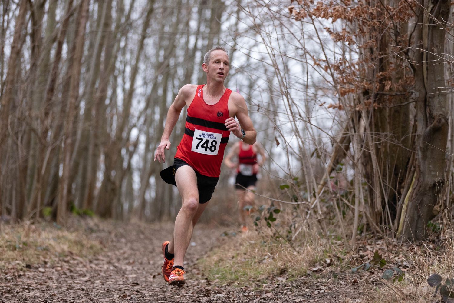 Trail runner in red singlet racing through autumn forest.