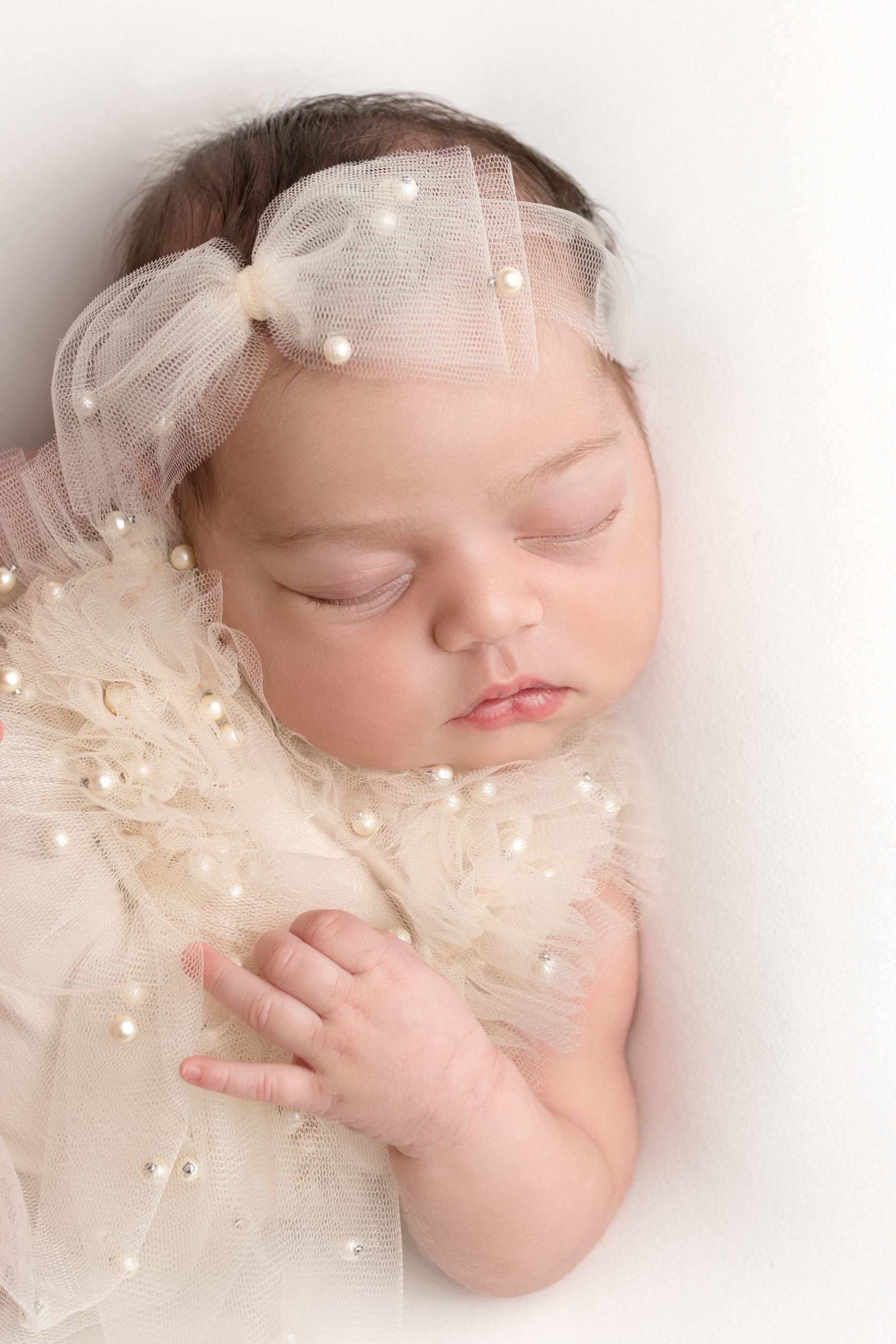 Newborn baby girl dressed in pearls and ivory tulle, asleep on her back, photographed by Pamela Clark