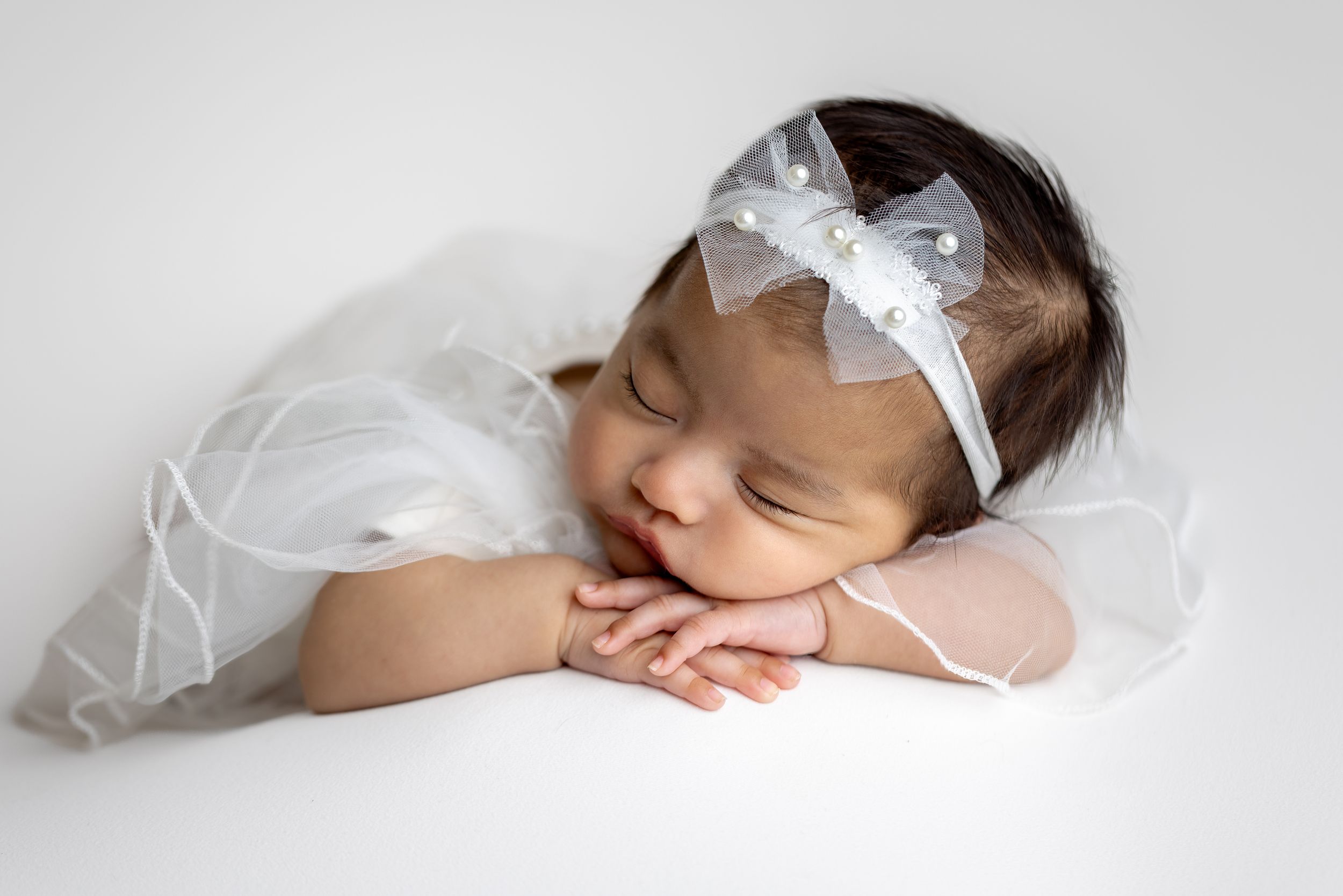 angelic newborn girl asleep, chin on hands, in all white