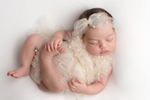 Newborn baby girl dressed in pearls and ivory tulle, asleep on her back in Huck Finn pose, photographed by Pamela Clark