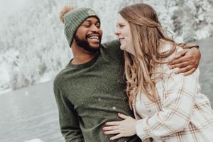 A happy couple smiles at one another in the snow in Olympic Peninsula, WA during an engagement session with Pamela Clark