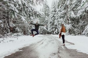 A man leaps after she said yes in the snow in Olympic Peninsula, WA during an engagement session with Pamela Clark