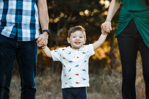 A young boy smiles as he hold Mom and Dad's hands during a photoshoot with Pamela Clark in Cedar Park, TX