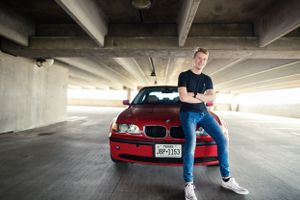 A high school senior sits on his BMW in a parking garage during his photography session with Pamela Clark