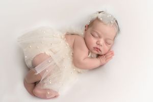 Newborn baby girl dressed in pearls and ivory tulle, asleep on her side, photographed by Pamela Clark