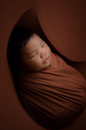 Newborn baby boy asleep on orange blanket, view from a side angle, posed in a moon bowl, photographed by Pamela Clark