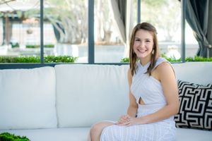 A high school senior sits on elegant outdoor patio furniture during her senior prom photoshoot with Pamela Clark