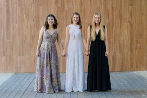 Three high school seniors dressed in prom dresses pose against a wooden wall during a photo shoot with Pamela Clark