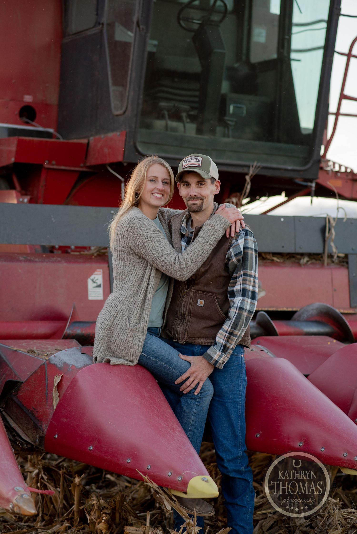 Couple posing together on the farming equipment during sunset.