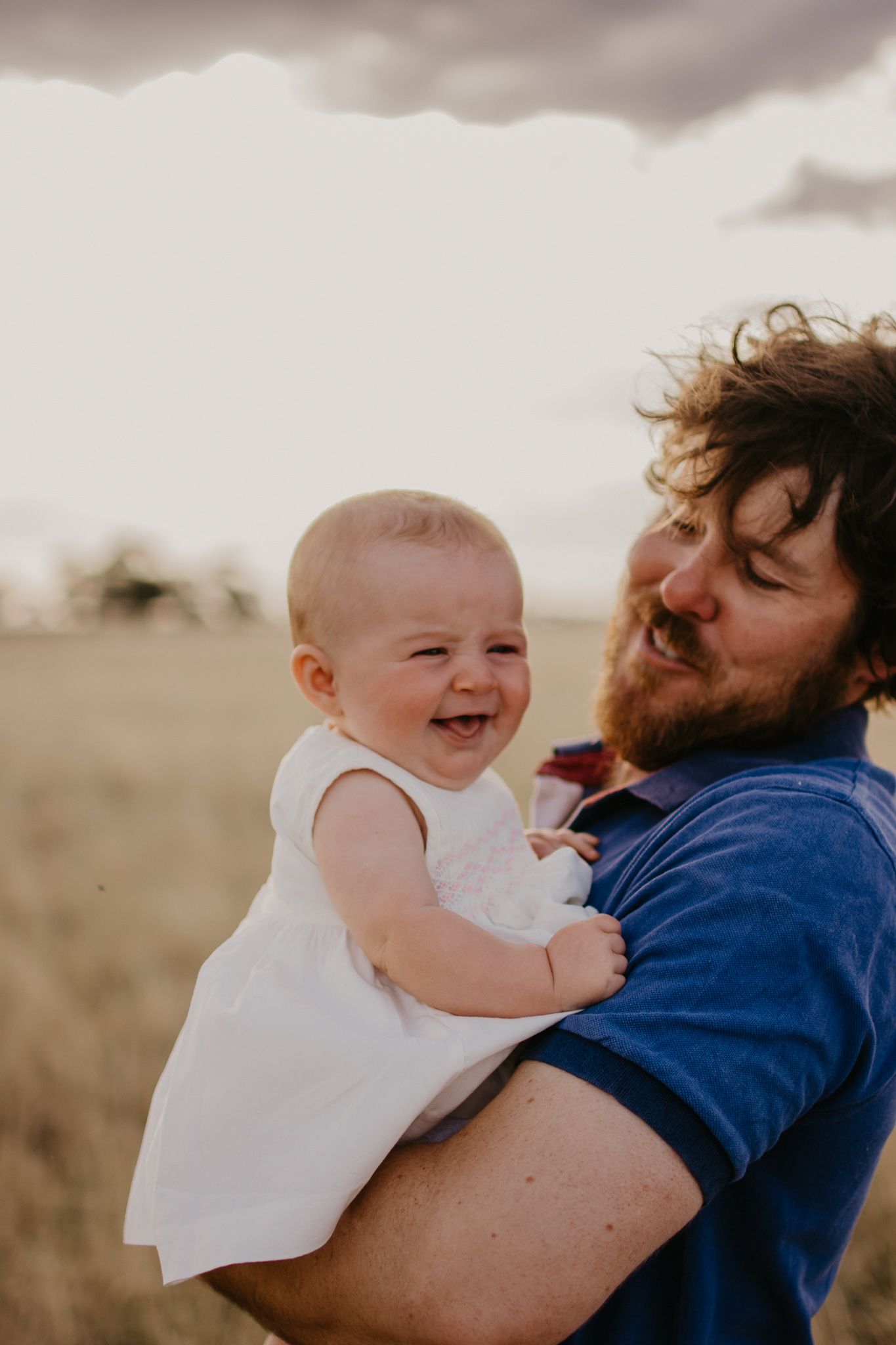 Dad and baby daughter, in the paddock, baby laughing and dad has a proud smile