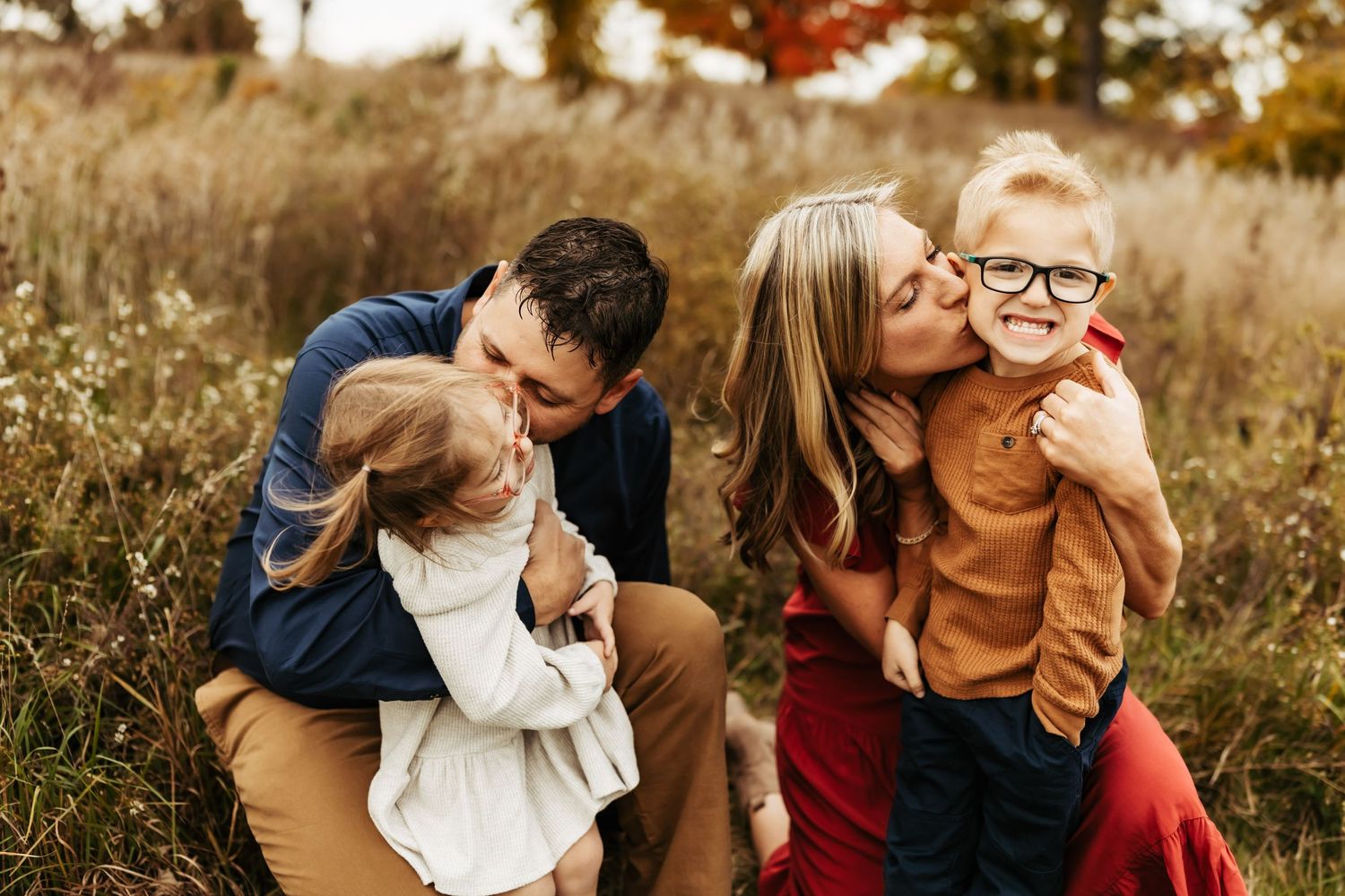 A warm family portrait session in a golden field during sunset, showing playful affection and love.