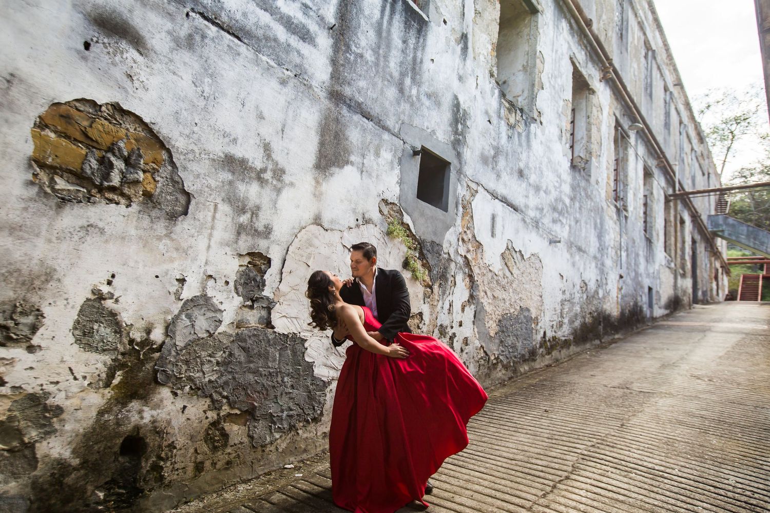 A flowing red dress adds drama against weathered white walls in an urban photo shoot.