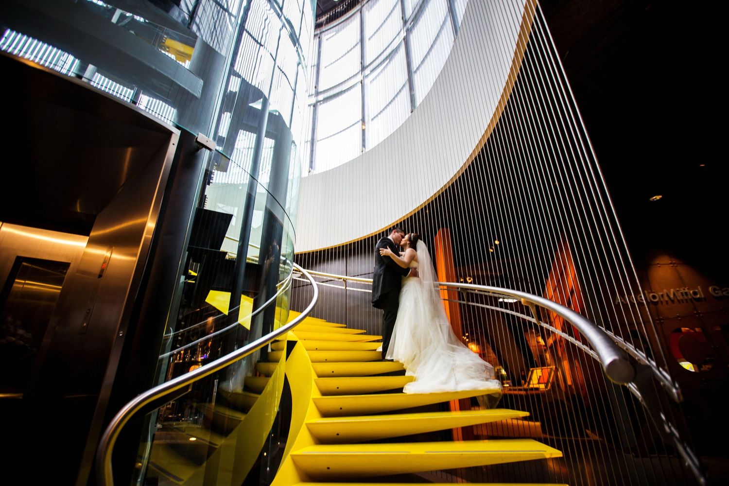 Wedding couple poses on modern yellow-lit staircase with sleek architectural details.