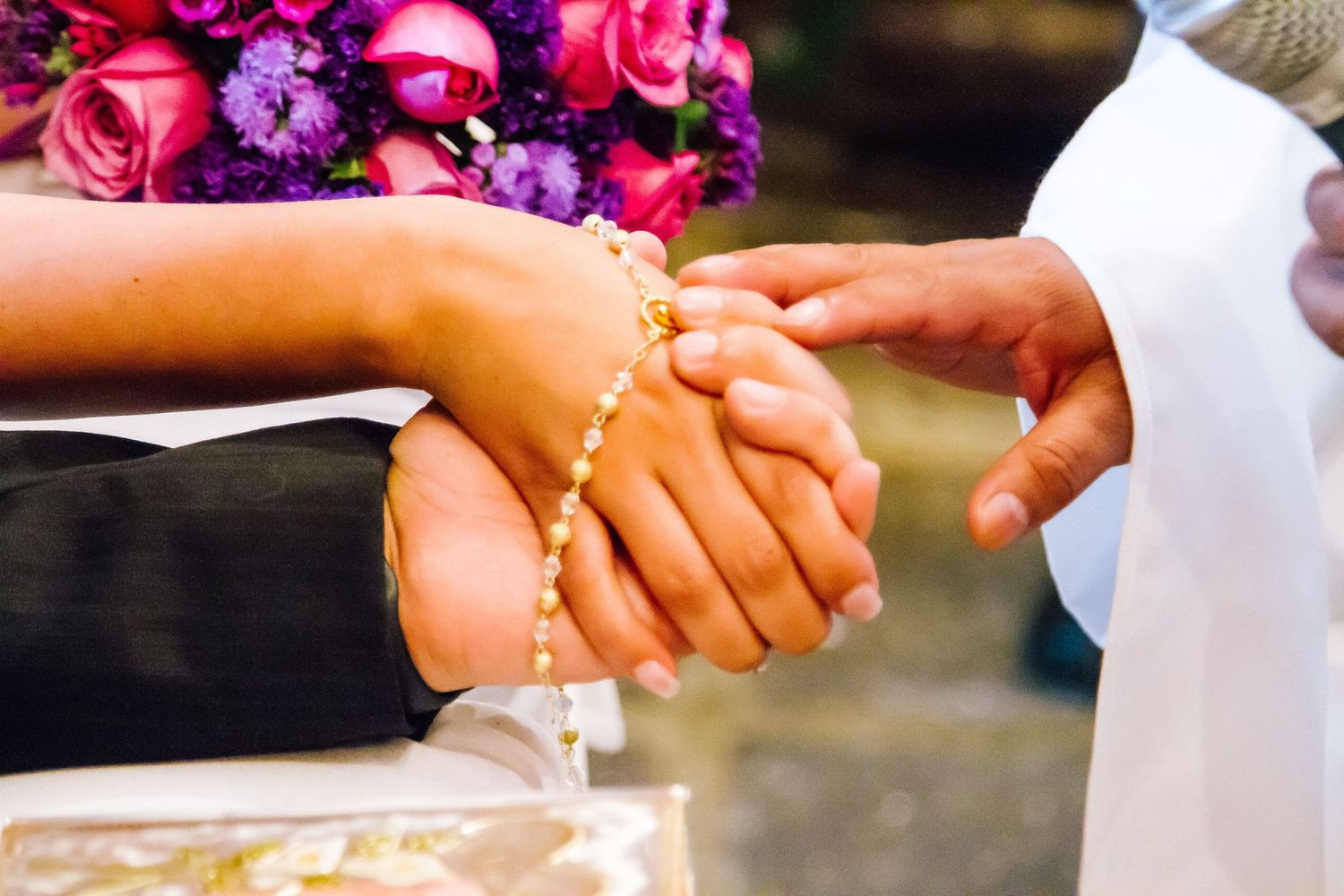 Close-up of hands exchanging rings with colorful flowers in the background.