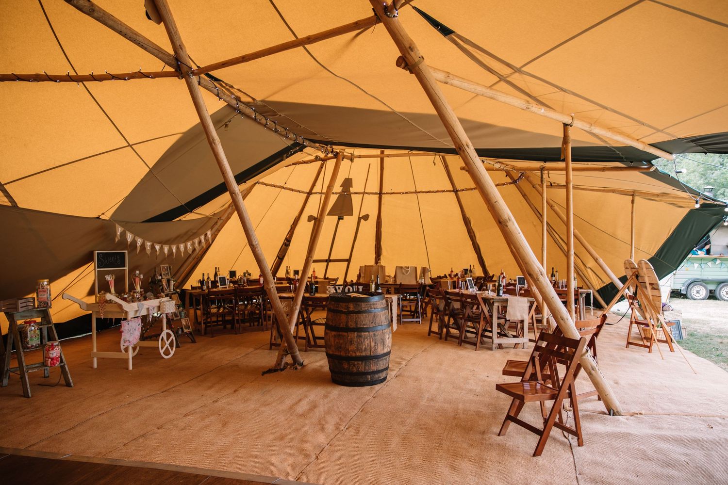 Interior of a spacious tipi wedding venue with wooden barrel tables and rustic decor.
