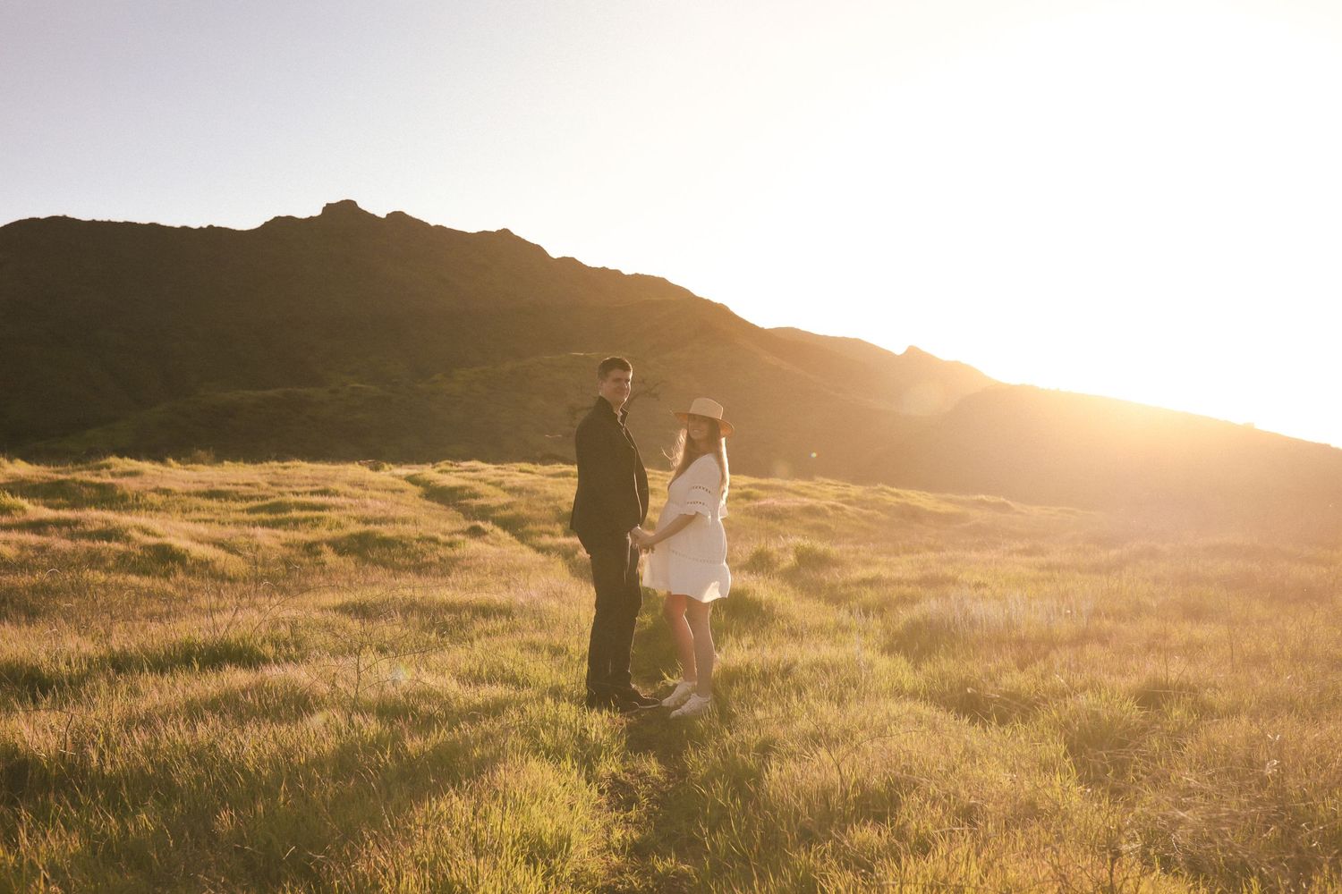 A romantic sunset silhouette of a couple embracing in a golden mountain meadow.