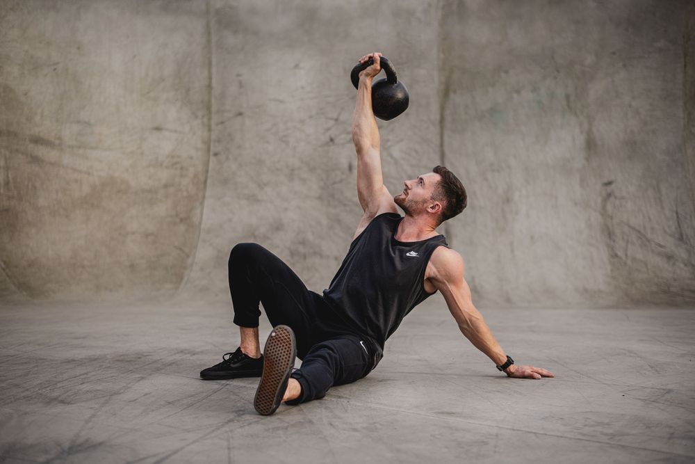 Athletic person performing Turkish get-up exercise with kettlebell on concrete floor.