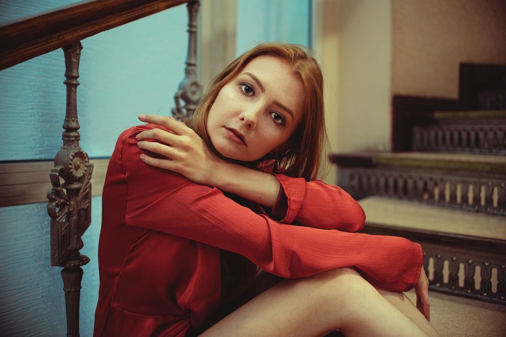 Dramatic poses in red attire against turquoise wall with ornate staircase railing.