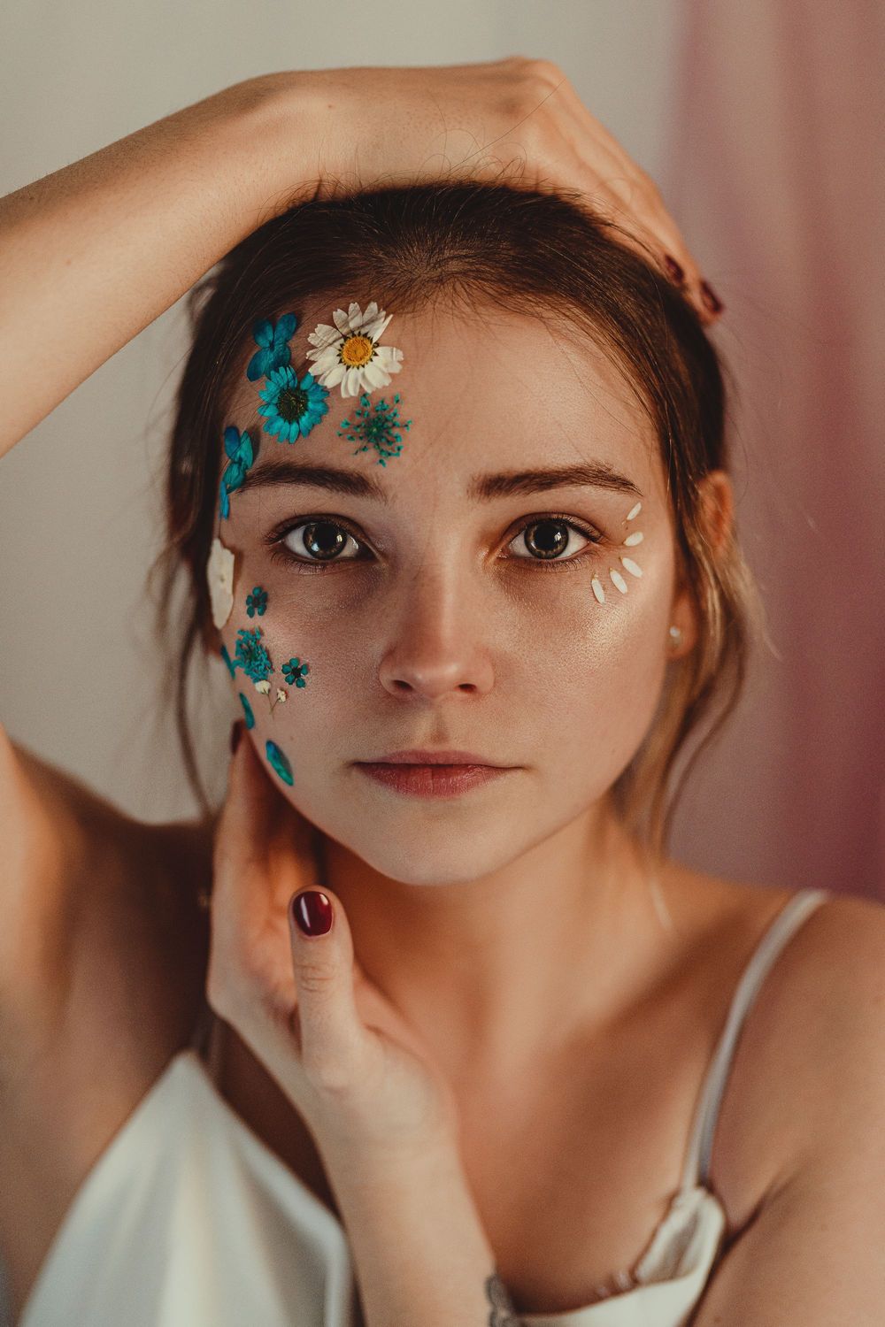 Creative portrait with blue floral face paint and artistic makeup details.