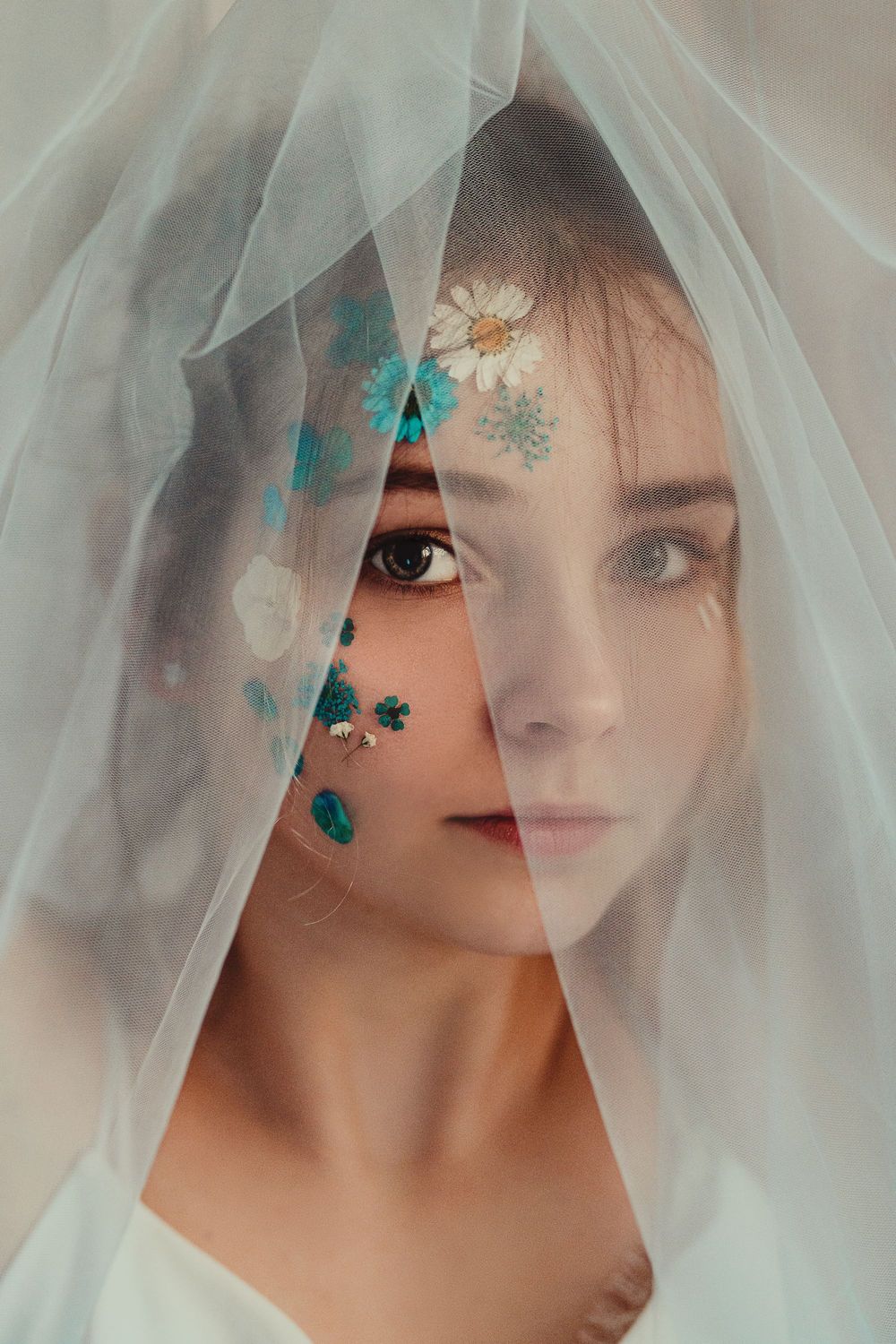 Ethereal portrait through sheer white veil with delicate turquoise floral details.