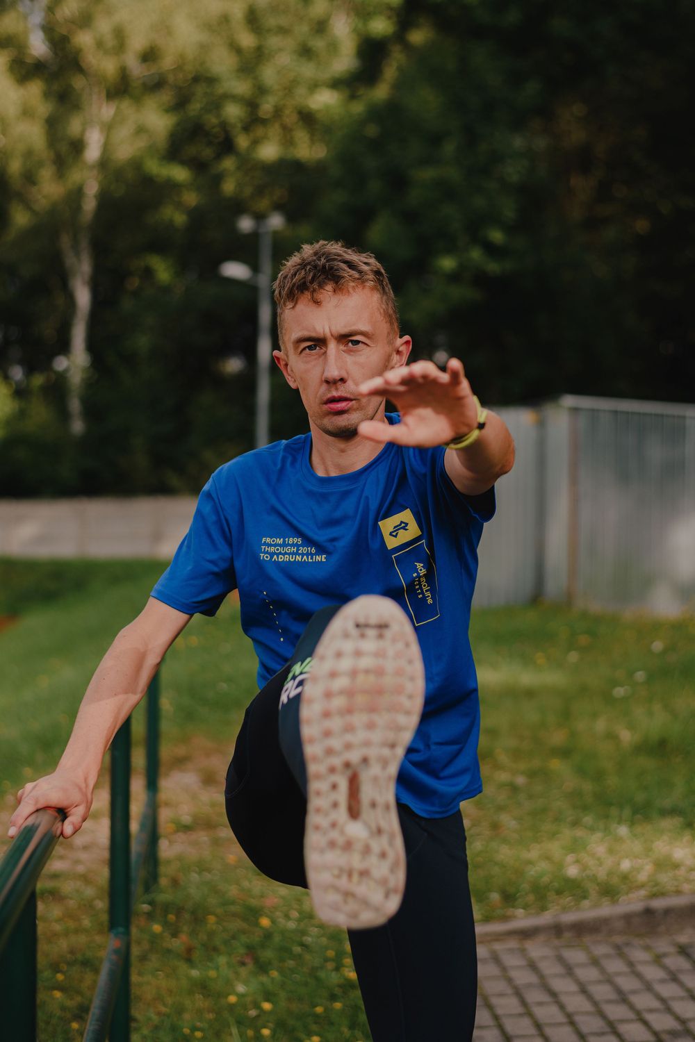Athlete in blue t-shirt demonstrating high kick stretch outdoors.