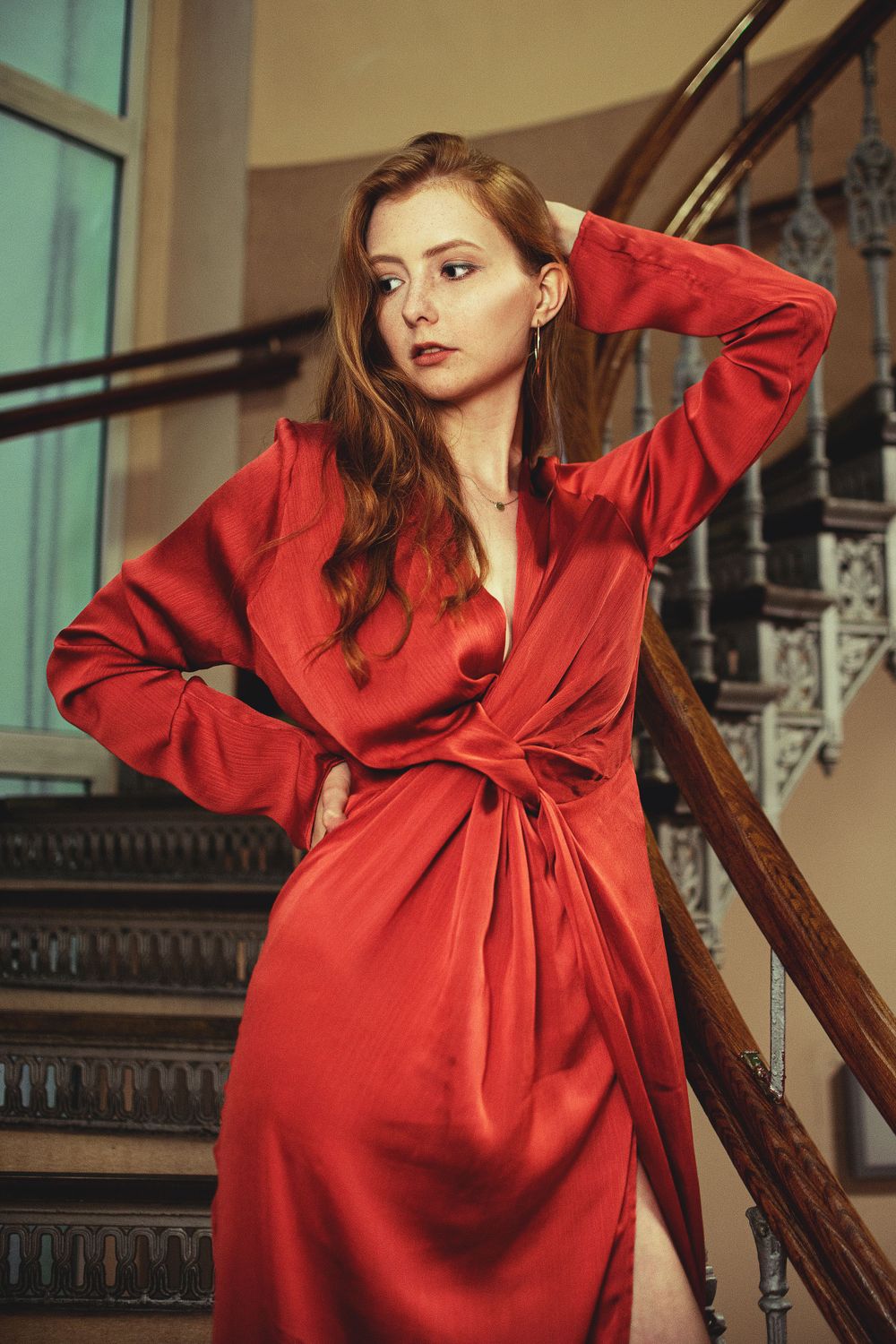 Fashion portrait on vintage staircase wearing flowing red wrap dress.